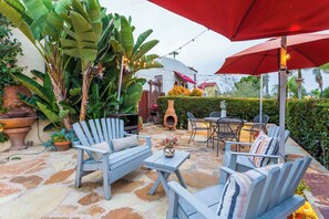 Un patio al aire libre con suelo de piedra, muebles de madera y un paraguas rojo.