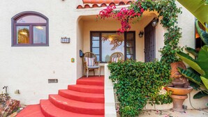 Uma casa com uma escadaria vermelha que leva a um alpendre com cadeiras de vime e uma mesa.