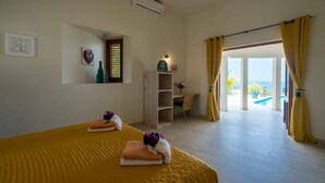A hotel room with two beds, a wooden cabinet, a small table with a vase, and a view of an outdoor pool. - Villa Vila Blenchi - Coral Estate (Rif. St. Marie)