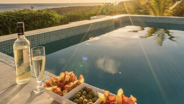 Et område ved poolen med en hvidvinflaske, et glas og forskellige snacks, blandt andet oliven, tomater og ost.