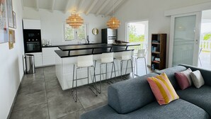 Et moderne køkken med en central ø, hvide barstole og hængende lamper.