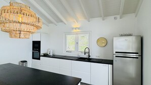 Et moderne køkken med hvide skabe, en sort bordplade, et rustfrit stål køleskab og en fletlysekrone.