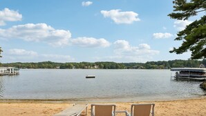 Vista de un lago con una playa de arena, sillas de descanso y un muelle con un bote.