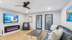 Una sala de estar con televisor de pantalla plana, chimenea, sofá de cuero y ventilador de techo.