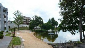 Un paseo junto al lago con un sendero de arena, rodeado de árboles y un edificio.