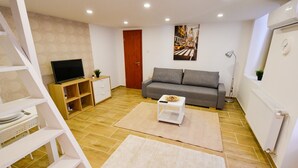 Ein modernes Wohnzimmer mit einer Couch, einem Flachbildfernseher, einem kleinen Tisch und einem Bild an der Wand.