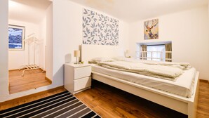 Ein Schlafzimmer mit Bett, Nachttischen, einem Wandbild und einem Fenster mit Vorhängen.