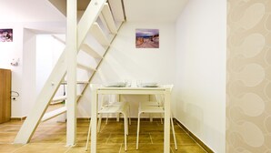 Ein Essbereich mit einem weißen Tisch und Stühlen, einer Treppe und einem kleinen Gemälde an der Wand.