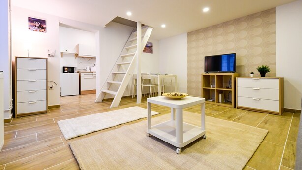 Ein modernes Wohnzimmer mit Küche, einer weißen Treppe, einem Flachbildfernseher und einem kleinen Tisch mit einer Schüssel.