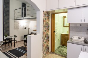A compact kitchen with white cabinets, a small dining area with a table and chairs, and a loft bedroom with a bunk bed. - Cosy studio flat, Síp street (Budapest)