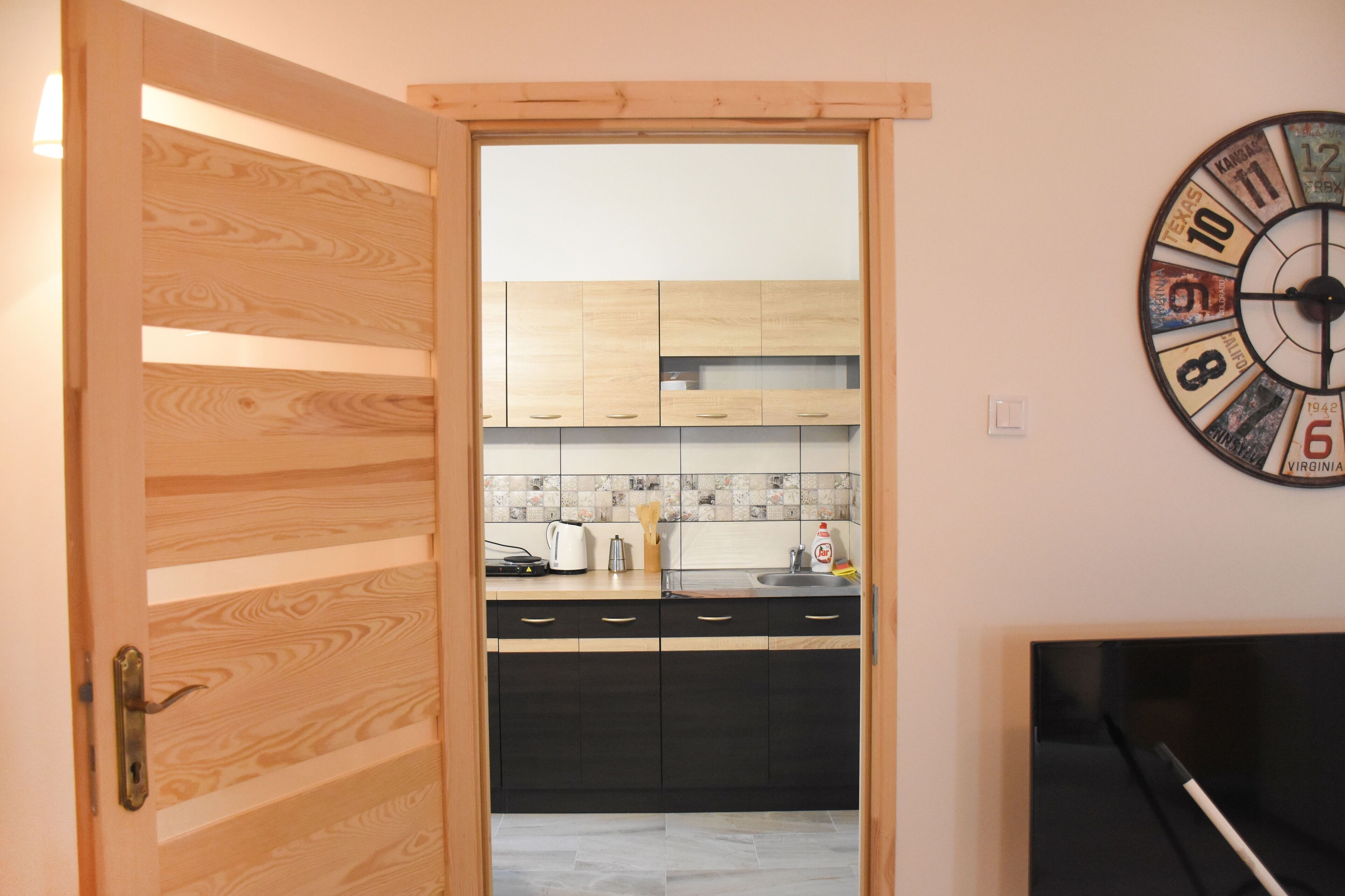 A kitchen with wooden cabinets, a tiled backsplash, and a wall clock.