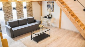 A modern living room with a gray sofa, a glass coffee table, and a white chair. A wooden staircase is visible in the background. - Cosy flat with balcony (Budapest)