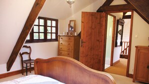 Quarto com cama de madeira, cômoda, cadeira e uma janela grande.
