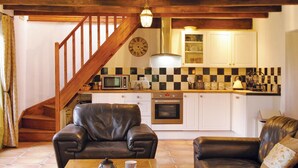 Uma sala de estar aconchegante com um sofá de couro, uma mesa de centro e uma escada que leva a uma cozinha com armários brancos e um painel de fundo quadriculado.