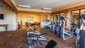 Ein Fitnessraum mit diversen Trainingsgeräten, Holzbalken und einem großen Fenster.