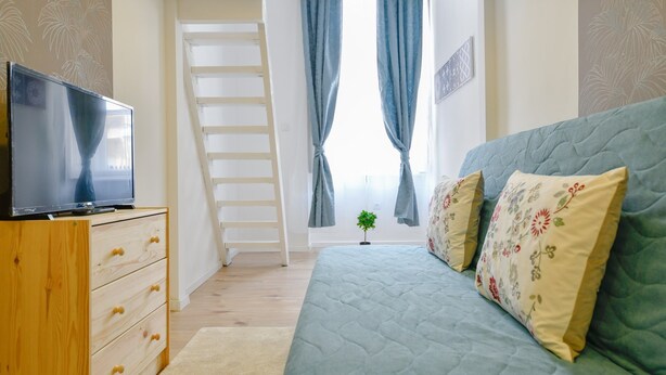 A bedroom with a bed, a TV on a wooden dresser, a ladder, and a small plant. - Cosy flat in Dob street, Juliet (Budapest)