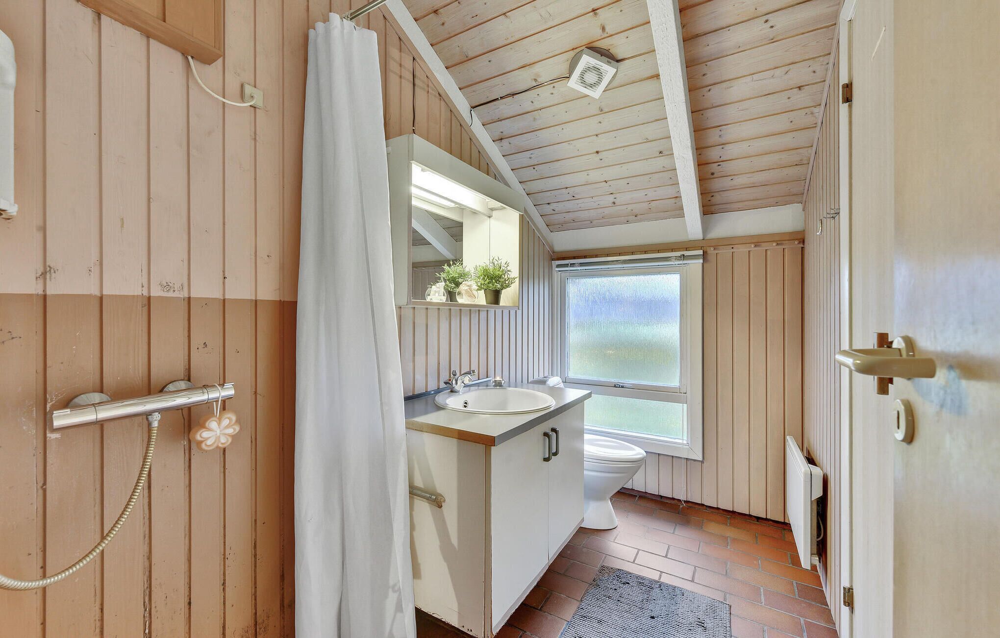 A bathroom with a wooden ceiling, a window, a sink, and a toilet.