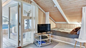 A cozy attic bedroom with a TV, a bed, and a sliding glass door leading to a balcony. - Amazing home in Hvide Sande with sauna (Hvide Sande)