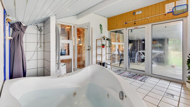 A modern bathroom with a large bathtub, a shower area, and a glass door leading to a patio. - Amazing home in Hvide Sande with sauna (Hvide Sande)