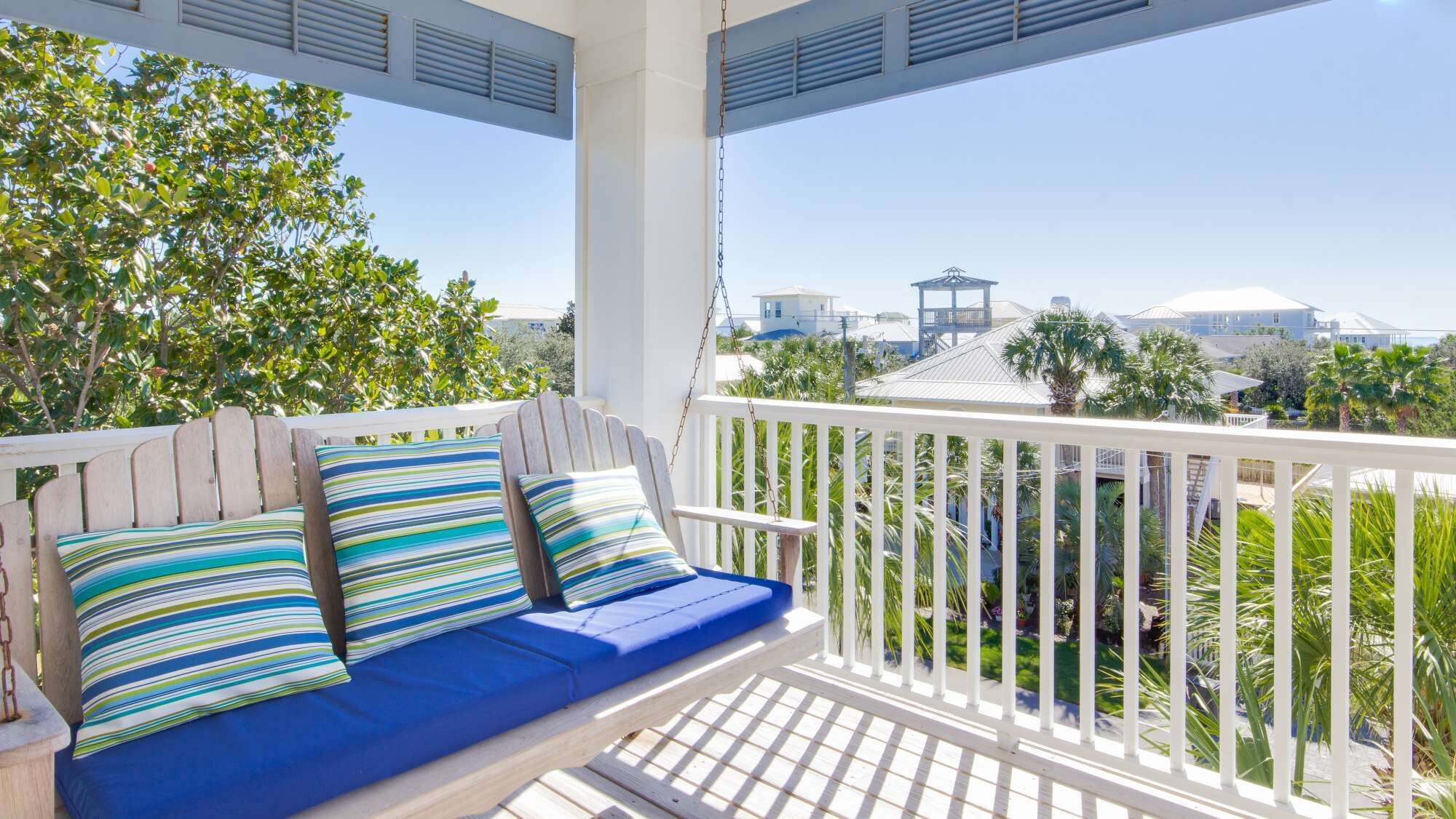 A covered outdoor seating area with a white railing, a blue cushioned bench, and striped pillows.