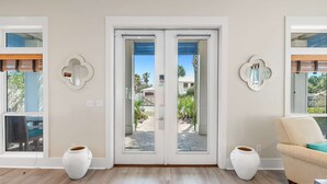 A room with a sliding glass door leading to an outdoor area, two wall-mounted mirrors, a wicker chair, and two white ceramic pots. - Gulf View - 30A Private Heated Pool, 3 min walk to the beach. No roads to cross. (Santa Rosa Beach)