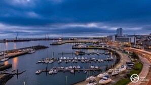 A marina with boats docked, a cityscape with buildings, and a clear sky. - Home Azores - Mountain View Apartment (Ponta Delgada)