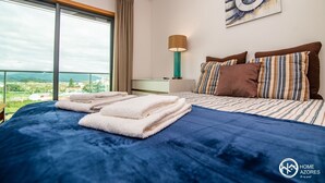 A hotel room with a large bed, a view of the city, and a painting on the wall. - Home Azores - Mountain View Apartment (Ponta Delgada)