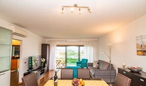 A modern living room with a dining area, a sofa, a TV, and a view of the outdoors. - Home Azores - Mountain View Apartment (Ponta Delgada)