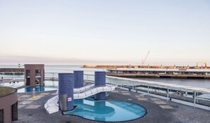 A rooftop pool area with a blue-tiled structure, a small building, and a view of the sea and port in the background. - Maison Açores - Apartment with a view of the mountains (Ponta Delgada)