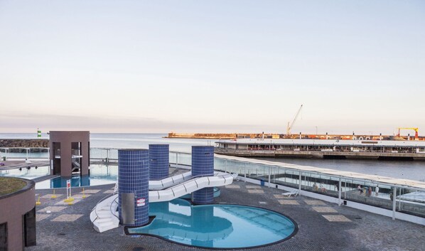 A rooftop pool area with a blue-tiled structure, a small building, and a view of the sea and port in the background. - Home Azores - Mountain View Apartment (Ponta Delgada)