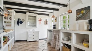 Cozinha com armários brancos, lava-louças embutida e janela com vista para área verde.