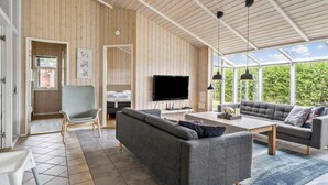Un salón amplio con un televisor grande, sofás grises y techo de madera.