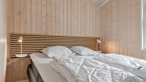 Un dormitorio con cabecera de listones de madera, dos lámparas de noche y una cama bien tendida con ropa blanca.