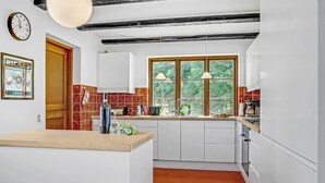 Une cuisine avec des meubles blancs, un plan de travail en bois, une fenêtre donnant sur un espace verdoyant et une horloge au mur.
