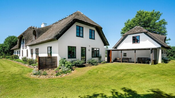 Une maison à deux étages, avec un toit de chaume, des murs extérieurs blancs et une pelouse bien entretenue.
