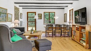 Un salon comprenant un canapé, une table basse, une table à manger, des chaises et un téléviseur. On y trouve également des étagères et une fenêtre donnant sur un paysage verdoyant.