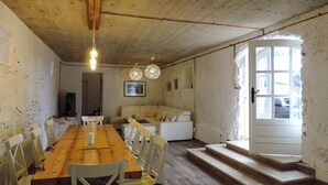 Un comedor rústico con una mesa y sillas de madera, un sofá blanco y una escalera que conduce a una puerta.