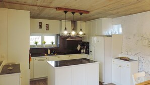Una cocina con armarios blancos, encimera negra y luces colgantes. Hay una ventana con plantas sobre la encimera, y un refrigerador a la derecha.