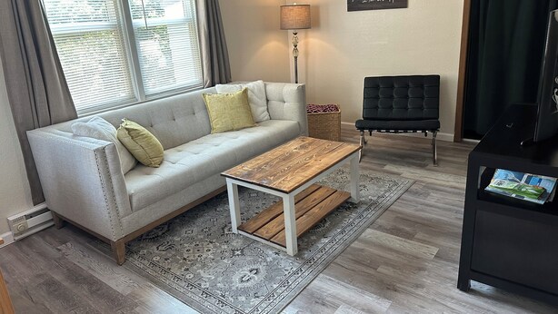 A living room with a sofa, a coffee table, a lamp, a black chair, and a TV stand.