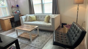 A living room with a sofa, a coffee table, a black leather chair, a lamp, and a desk with a chair.