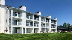 A multi-story hotel with balconies, a flat roof, and a well-maintained lawn. - Waterfront Setting w/ Top-Floor Views Overlooking Lake Charlevoix (Charlevoix)
