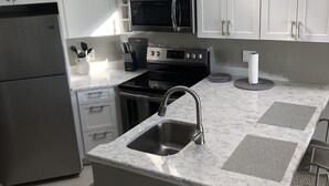 A modern kitchen with white cabinets, stainless steel appliances, and a marble countertop. - Waterfront Setting w/ Top-Floor Views Overlooking Lake Charlevoix (Charlevoix)