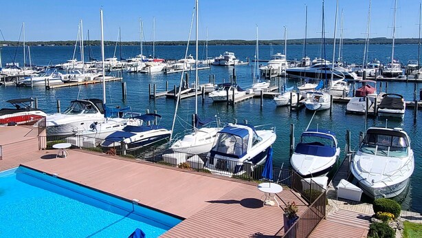 A marina with boats docked, a swimming pool, and a wooden deck with seating. - Waterfront Setting w/ Top-Floor Views Overlooking Lake Charlevoix (Charlevoix)