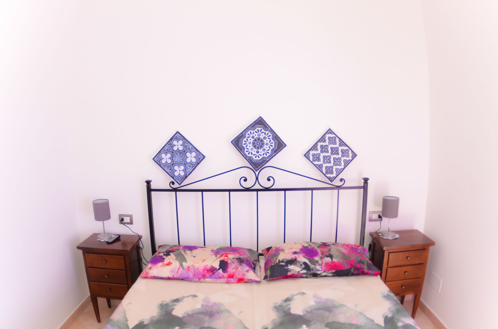 Un lit avec une literie à motifs floraux, une tête de lit en métal et des éléments décoratifs muraux.