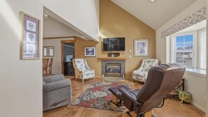Un salon avec une cheminée, deux fauteuils, un canapé et un téléviseur.