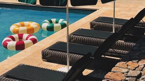 Un espace aménagé au bord de la piscine, avec des chaises longues et des parasols, entouré de la piscine et de verdure.