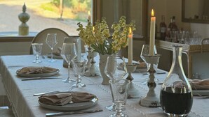 Une table à manger dressée avec une nappe blanche, de la verrerie, des bougies et une bouteille de vin.