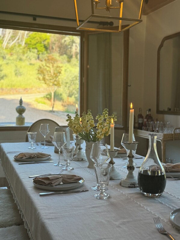 A dining table set with white tablecloth, glassware, candles, and a bottle of wine.