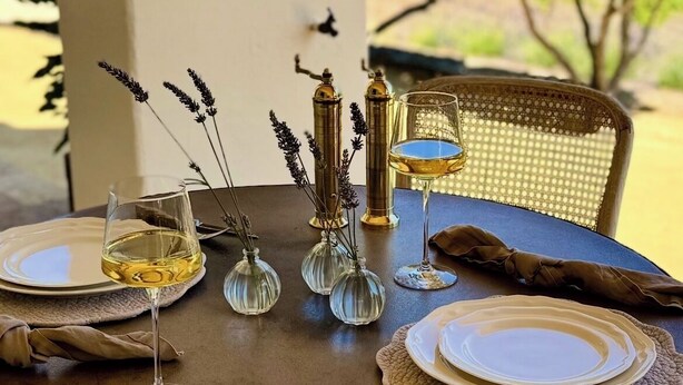 Une table ronde dressée pour deux personnes, avec des verres à vin, des couverts et des vases décoratifs.
