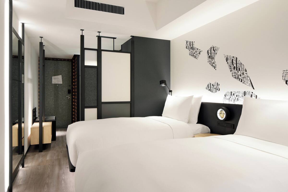 A modern hotel room with two beds, a desk, and a large window.